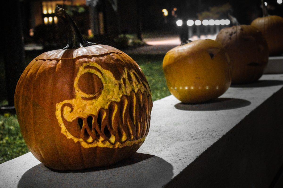 Calabazas de Halloween talladas sobre un muro de noche; en primer plano, una con cara de monstruo y dientes afilados